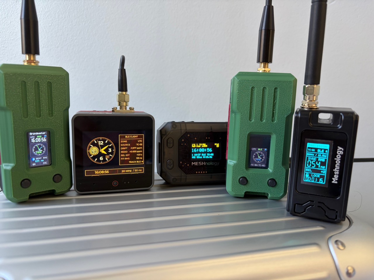 Five antenna-equipped PToB development clocks with illuminated displays on a metal bench.